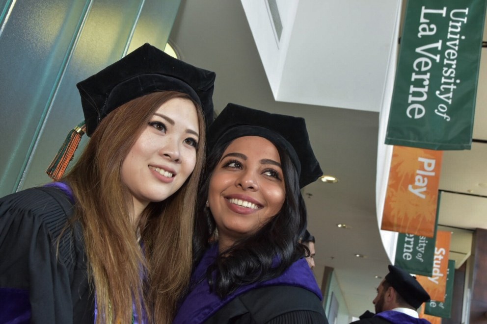 Female students smile in the Michael and Sara Abraham Campus Center after graduation.