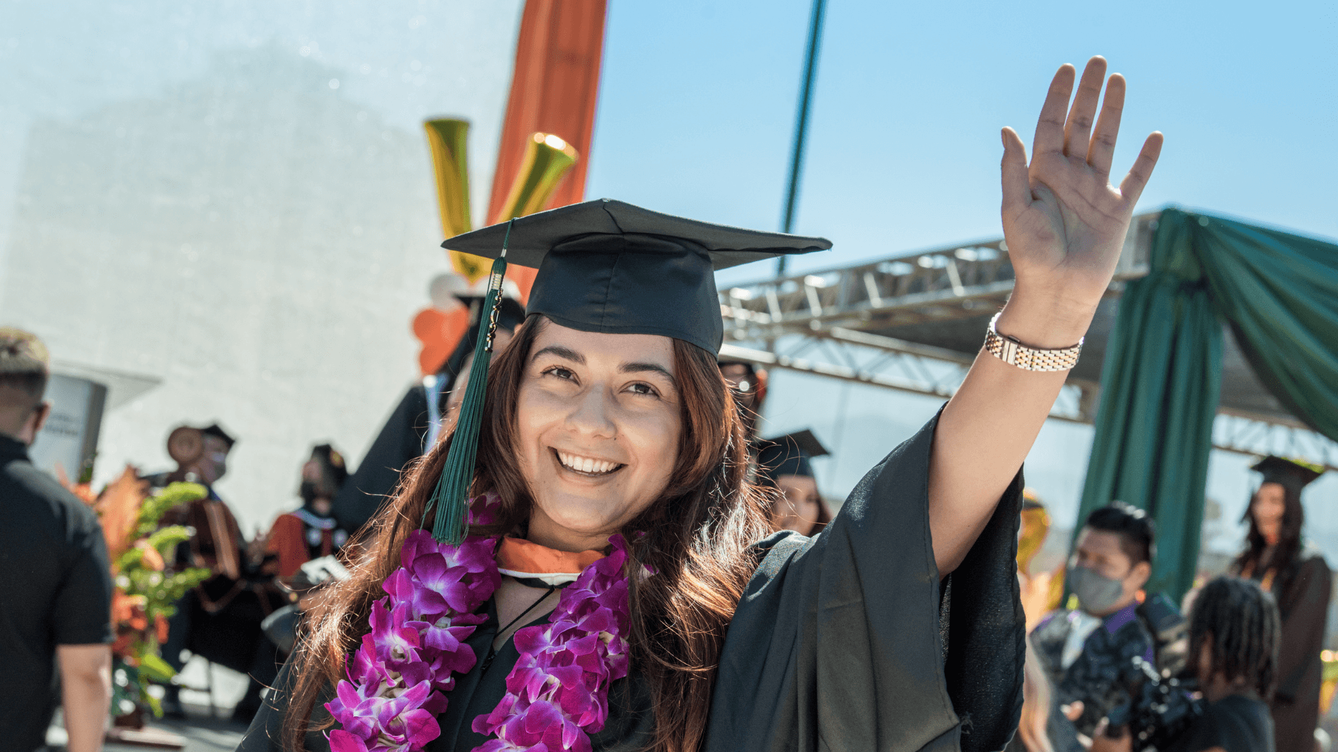 New graduate waving at San Manuel Stadium in-person graduation ceremony