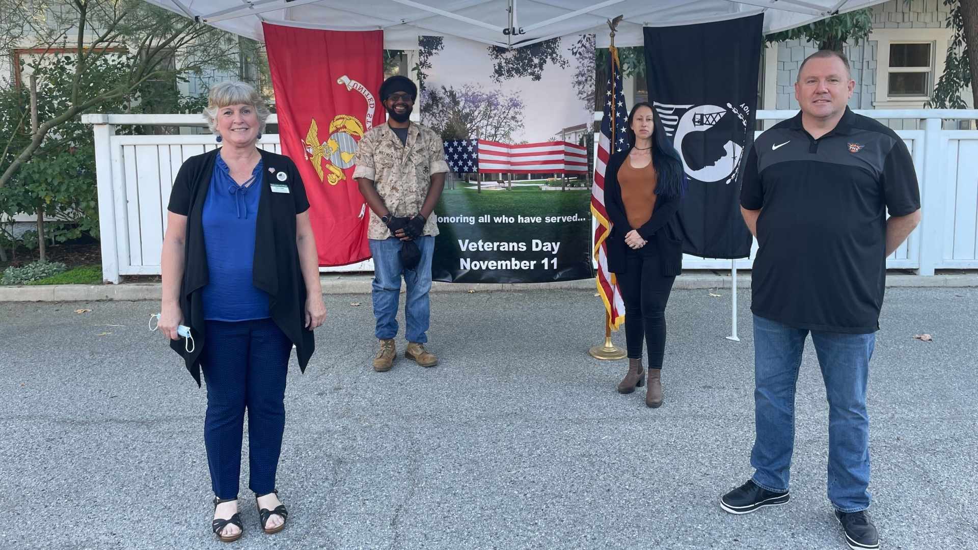 Four military veterans standing next to American flag and military flags with Veterans Day signage at the University of La Verne