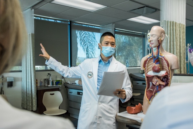 A faculty member in a lab coat instructs students in the physician assistant program.