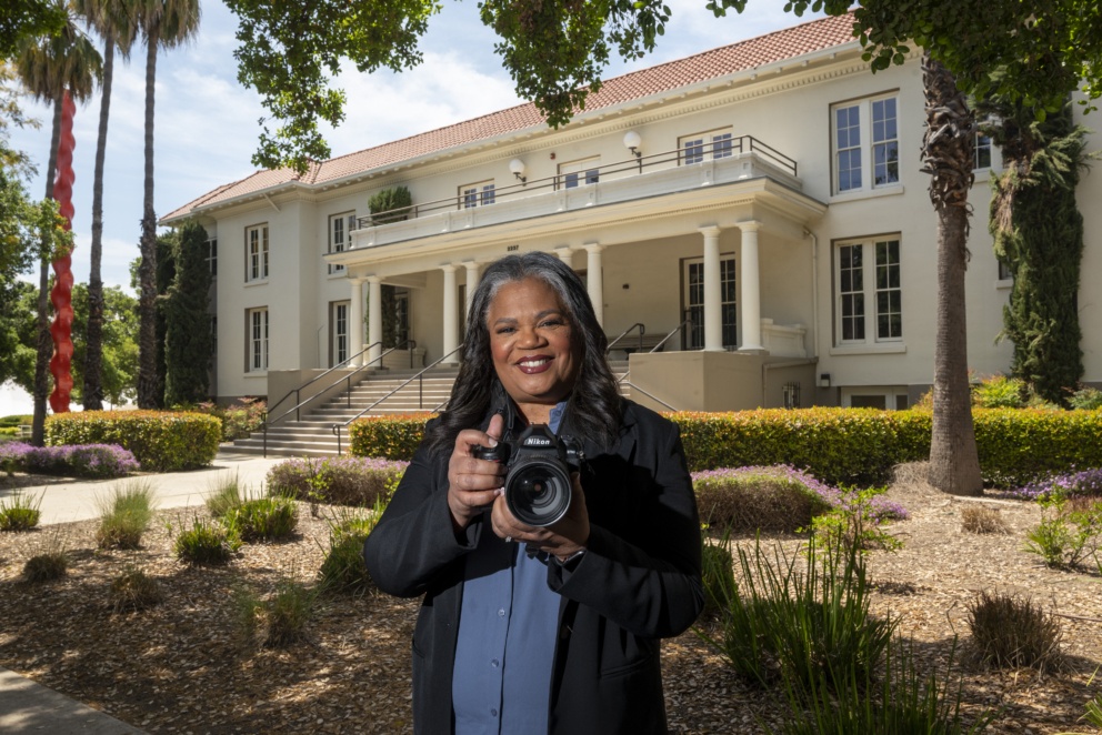 Darcelle Jones-Wesley is a graduate of 2023 standing in front of Miller Hall with her camera.