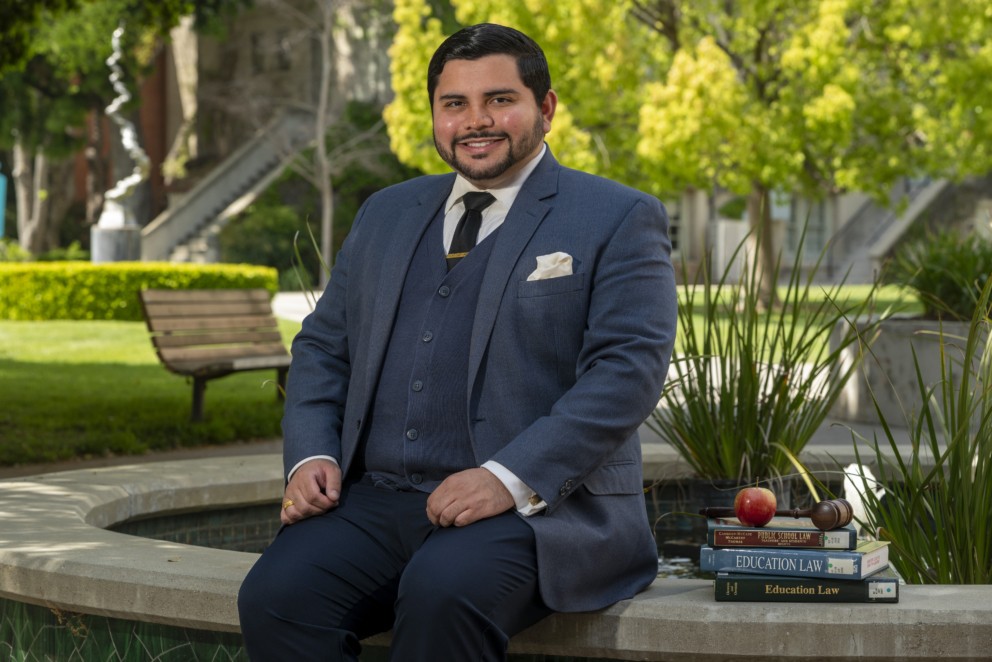 Jeffrey Torres, graduate of 2023, sits in front of a fountain on campus