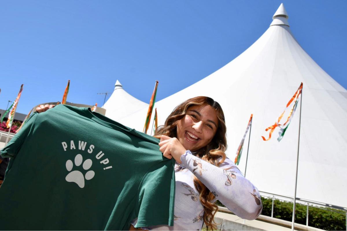 Convocation 2023 - student holding paws up shirt in front of Tents for Convocation ceremony