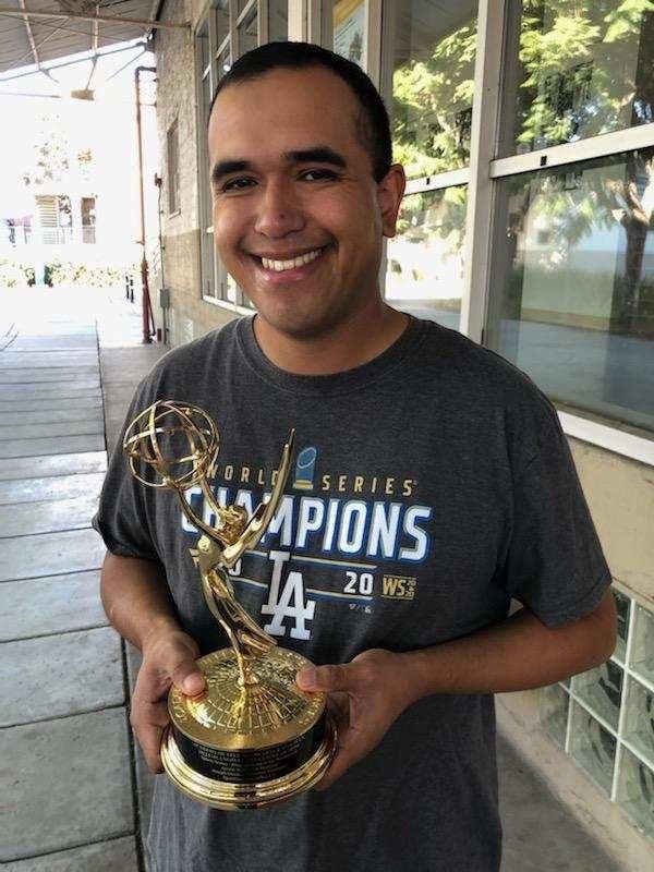 Alumnus Joseph Orozco stands with Emmy award in hands in front of ACB building on campus