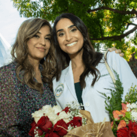 2023 White Coat Ceremony student smiling with parent outside with flowers