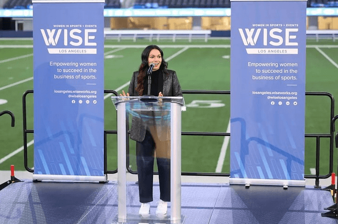 alumna danielle garcia speaking in sofi stadium at a podium for women in sports leadership event